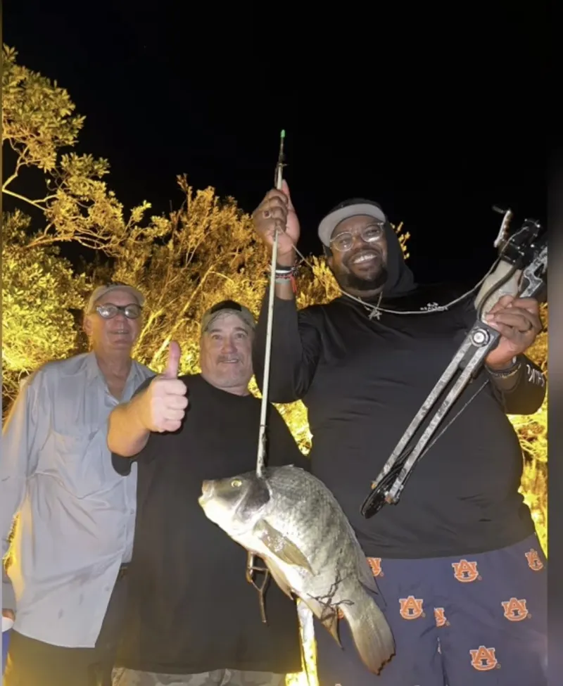 Three of the night's crew holding up a fish under the lights